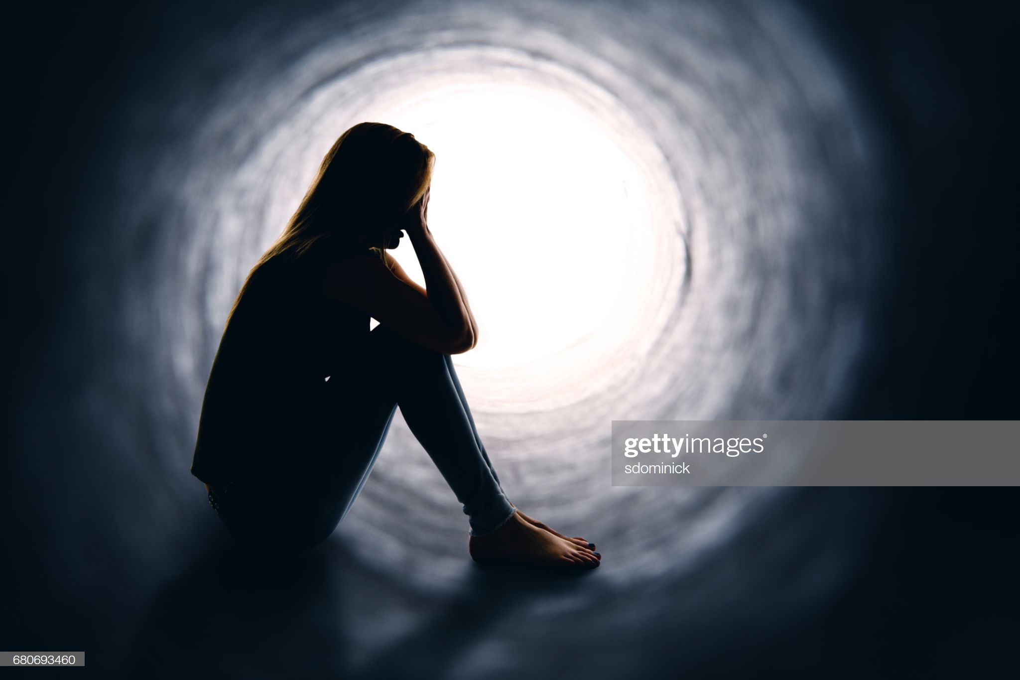 A depressed woman sitting alone is a dark tunnel with light at the other end.