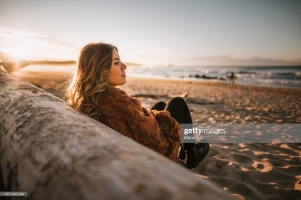 Young woman sitting by a beach at sunset in winter